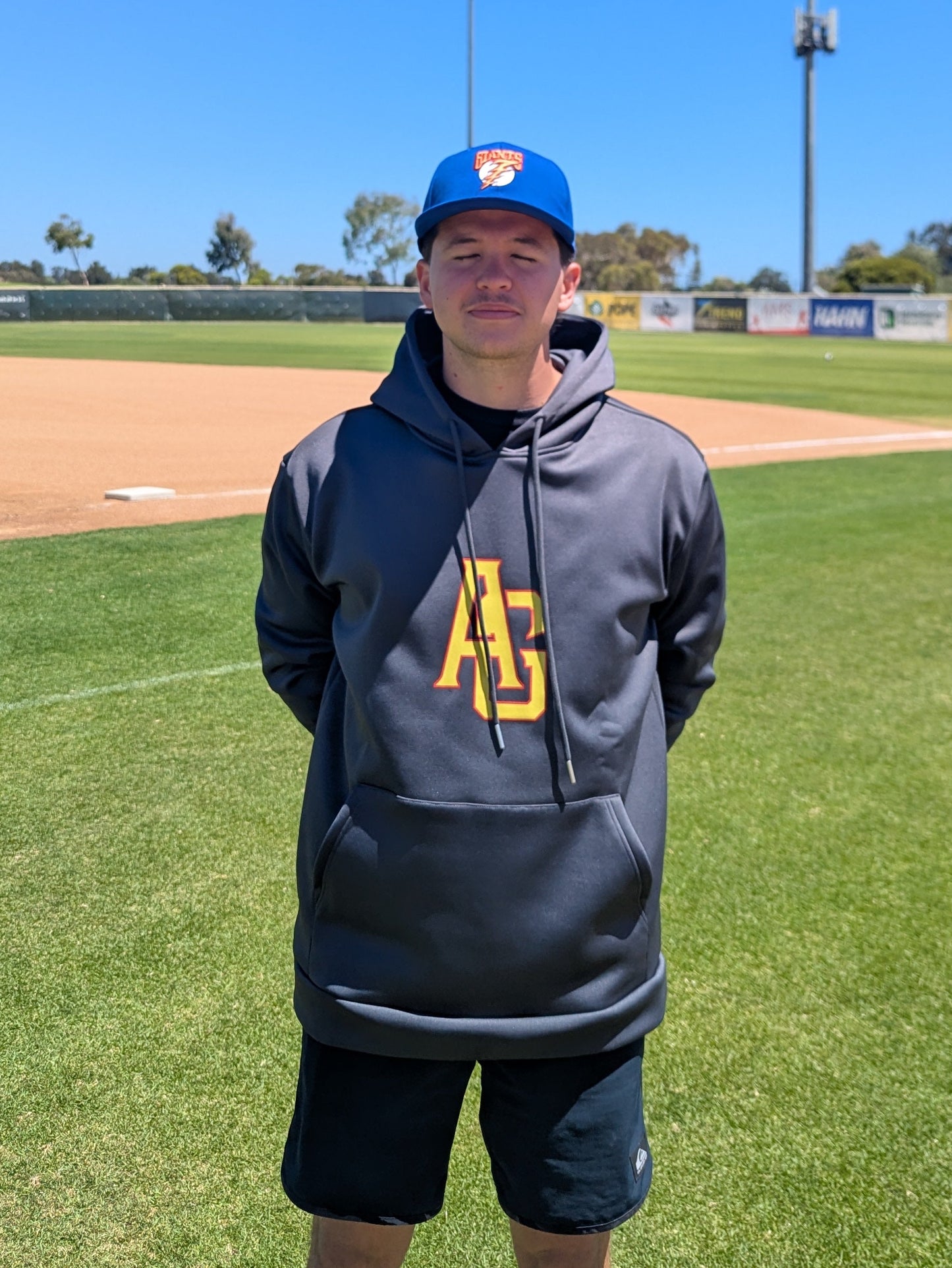 Person wearing a hoodie and cap on a baseball field with clear blue sky